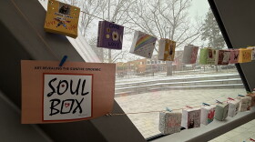 Photo shows several small origami boxes hung along a string across a window. Each box is directed to honor victims of gun violence.
