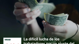  En la imagen se puede observar dos manos contando un paquete de billetes de dolares estadounidenses. Las manos son de una persona blanca. En el lado inferior de la imagen esta el logo de Que Onda Michigan sobre un fondo blanco. En la parte derecha las siguientes palabras estan escritas: "La difícil lucha de los trabajadores por un ajuste del salario mínimo en Michigan." En el lado superior de la imagen se encuentra las pablaras "WKAR" en color blanco.  y "Episodio 93".