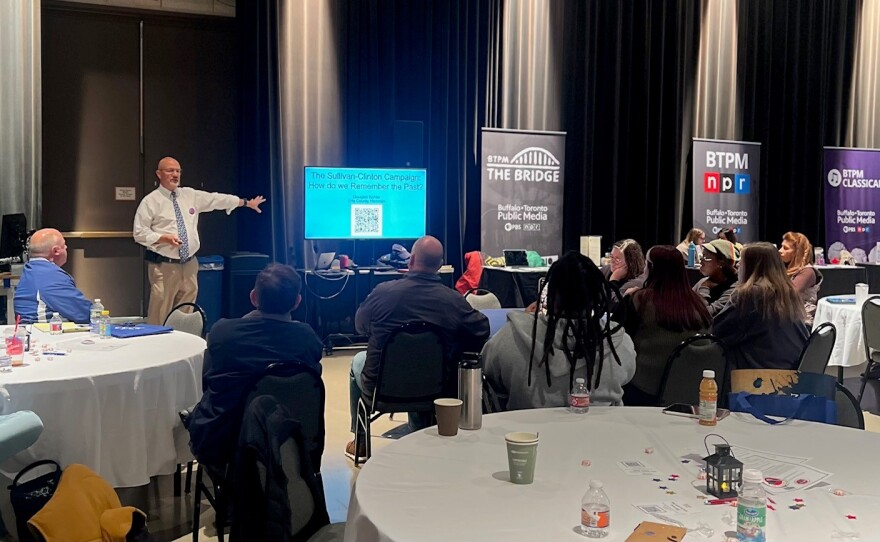 Doug speaking to the audience and using a TV for a powerpoint.