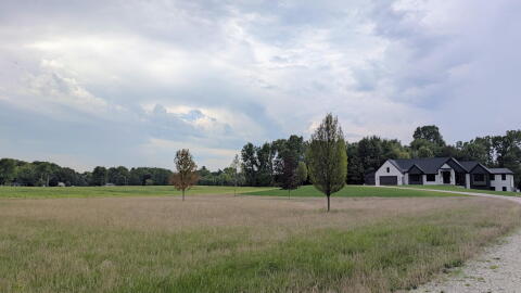 A house is seen at the end of a gravel driveway with a large field to the left of it