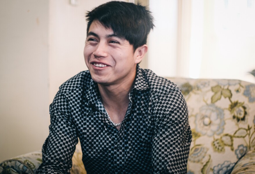 English: A photo of a young man sitting in a chair and smiling. Español: La foto de un hombre joven sentado en una silla y sonriendo.