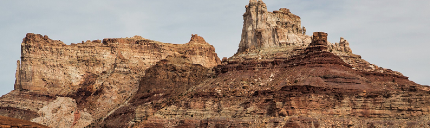 A large mountain stands out against the desert. It is red and orange and gray and white and there are numerous rock layers