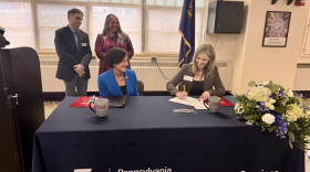Kimberly Tenbus, CEO of Clarks Summit State Hospital (right), signs the clinical agreement while Pa. Human Services Sec. Val Arkoosh (left, seated), Dr. Ryan Smith, the associate dean of clinical affairs and graduate medical education at IUPCOM (standing left) and IUPCOM's founding dean Dr. Miko Rose watch.