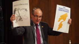Sam Dunklau / WITF House Majority Leader Kerry Benninghoff (R-Centre) holds up a map of a proposed state House district and compares it to another political cartoon demonstrating a “well-fed lizard” gerrymander on at an LRC meeting on Dec. 16, 2021