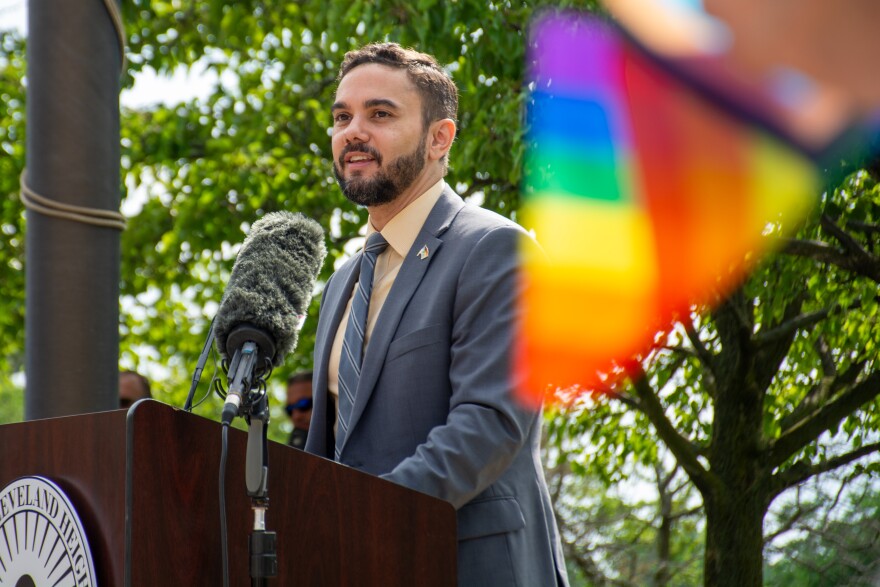 Cleveland Heights Mayor Kahlil Seren speaks from a lectern. An LGBTQ pride flag flies in the foreground.