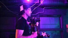 Two people side by side in profile holding cameras in a dark space