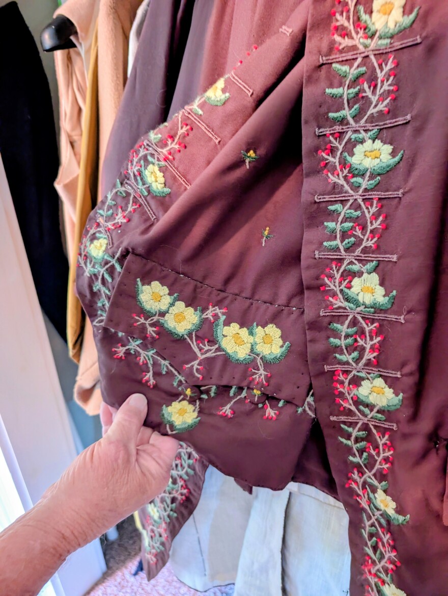 Paul Brennan holds up a coat with floral embroidery along the edges. 