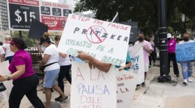  People walk down a sidewalk carrying signs advocating for the continuation of healthcare coverage for undocumented immigrants.