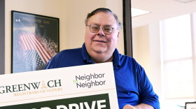 Republican Registrar of Voters Fred DeCaro III holds up a sign promoting a food drive by Neighbor to Neighbor, a local nonprofit that also has a donation bin at Greenwich Town Hall during early voting on October 20th, 2026. DeCaro said he's already received a full bin of donations since the drive commenced on Monday.