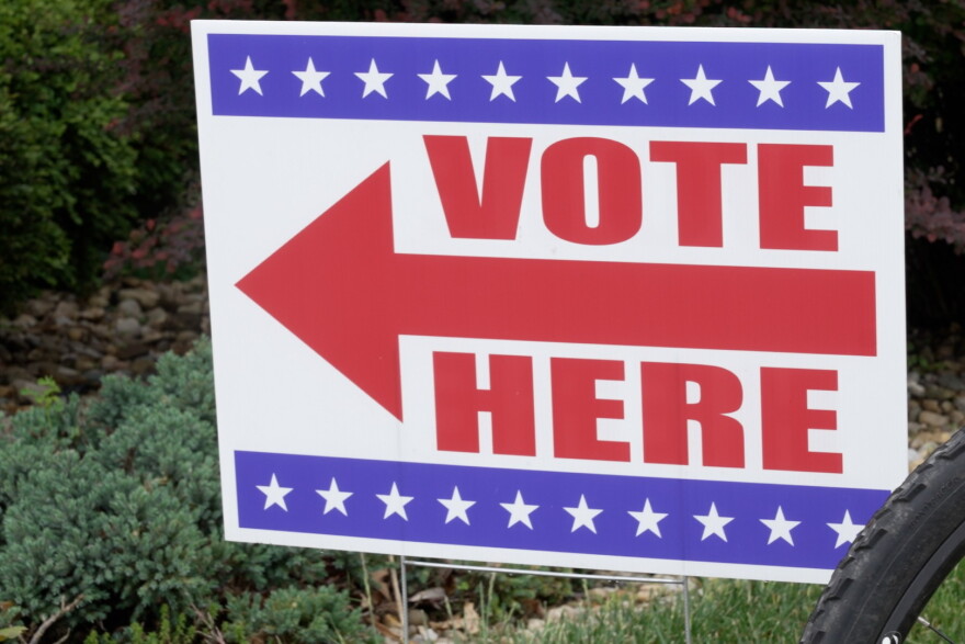 A red white and blue sign with an arrow that says "vote here"