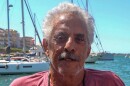 Bob Suberi stares directly at the camera. Boats and water visible behind him.