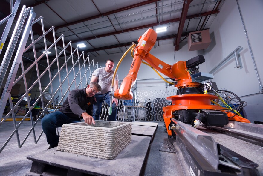 At the Quad Cities Smart Design and Manufacturing Lab in Davenport, lab director Eric Faierson (kneeling) and an Iowa State graduate student conducting research on additive construction (3D) while using robotics.