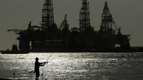 FILE - A man fishes near docked oil drilling platforms May 8, 2020, in Port Aransas, Texas. 