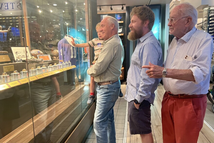 From Left: Jonas Wheeler, 4, Tac Justi, 66, Matt Wheeler, 39, and Henry K. Justi, 92, view the opening display case at Spurrier’s. Steve Spurrier’s 1966 Heisman Trophy, championship rings, jerseys and more are shown in the large display. (Keira Shoaf/WUFT News)
