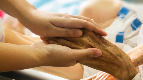 A person holding the hand of an elderly person.