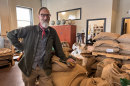 A man stands next to dozens of large burlap bags full of coffee beans. 