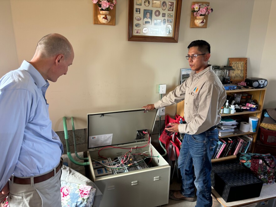 Navajo Power Home technician Jeremy Begay shows U.S. Department of Energy Deputy Secretary David Turk the battery storage unit inside Nolan and Sarah Huskon's hogan, which received power for the first time in June 2024 via an off-grid solar system from the company.