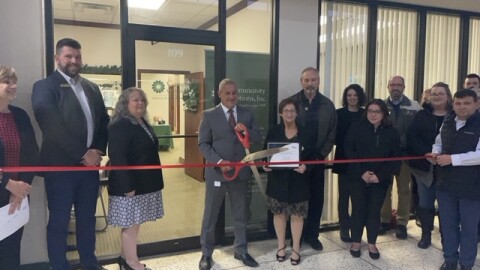 A group of people stand outside the Council Bluffs office. They are cutting a red ribbon.