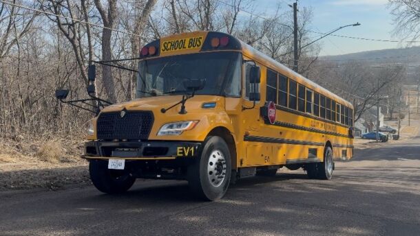 A yellow school bus is climbing a hill. There are many trees without leaves to the left of the bus.