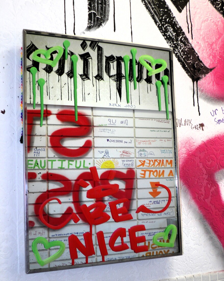 A piece of art on a wall, message written in red says "Be Nice"