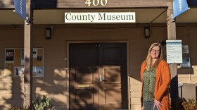 A woman stands outside a building with wooden double doors and a sign that says, "County Museum."