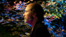 Musician Brian Bacon poses in front of a piano in a half-silhouette 
