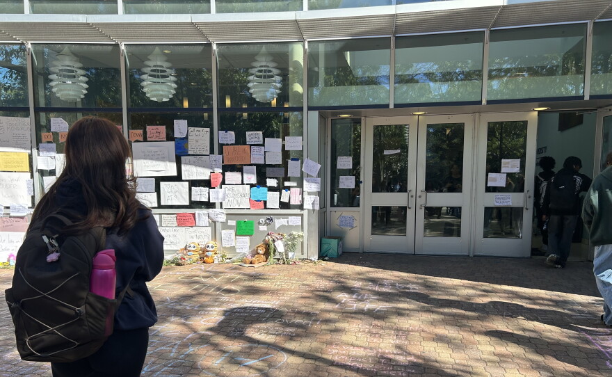 A student stands outside the Batten Arts and Letters building at Old Dominion University on Oct. 26, 2026, looking at signs and other tributes left as a memorial for a student who died at the building the week before.