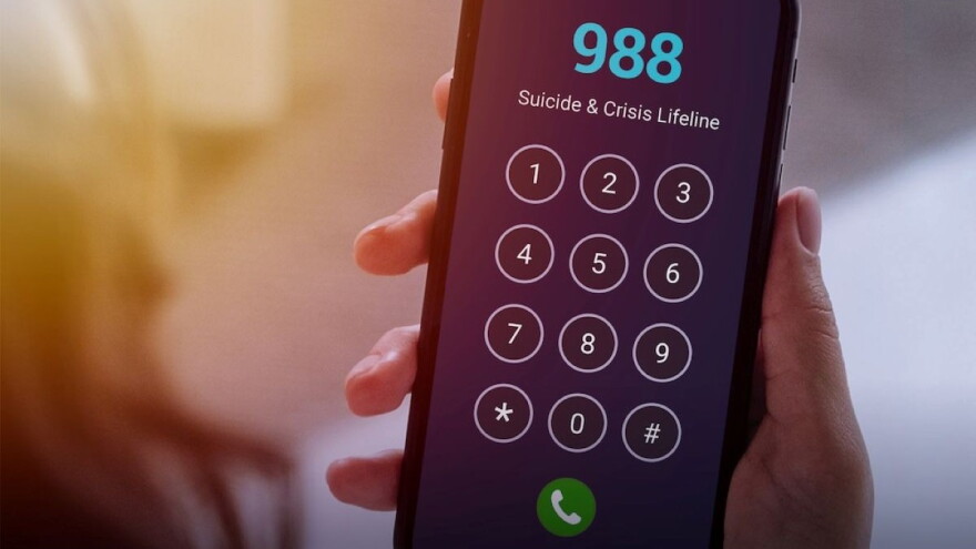 a hand holds a cellphone that is dialing 988