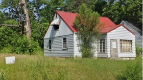 A house sits vacant and boarded up in the 1700 block of North Johnson Street in South Bend, next to a vacant, overgrown lot.