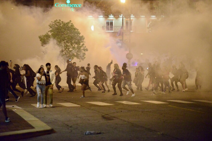 People scatter amid a cloud of tear gas during demonstrations Saturday night at Kansas City's Country Club Plaza.