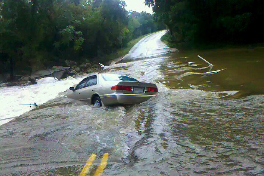 A car is partially submerged underwater along a road that has been flooded.