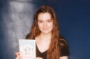 A woman with long brown hair holds a copy of the book "You Don't Need a Smartphone." Several copies of the book are splayed out on a table in front of her. 