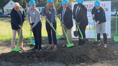 Six people holding green shovels break ground at a construction site