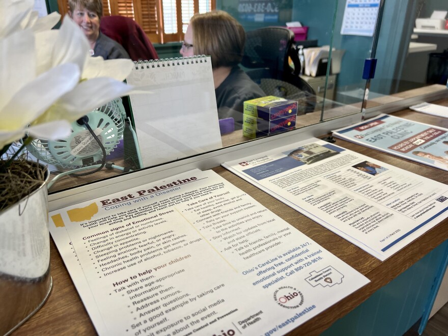 Handouts on how to cope with disaster sit on the counter at the East Liverpool City Hospital clinic in East Palestine. In the background, two women sit at the check-in desk smiling at one another.