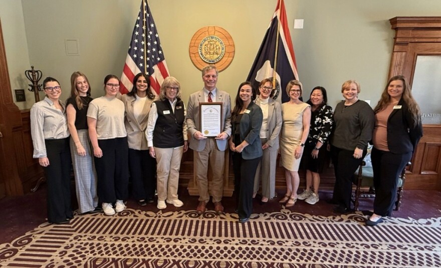 A man holding a plaque stands amid a line of women in front of the U.S. and Wyoming flags.
