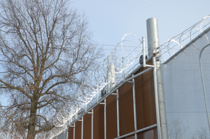 Chicken wire is laced on the top of a metal fence.