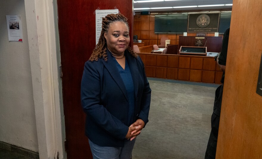 A woman in a blue blazer stands in front of an office door 
