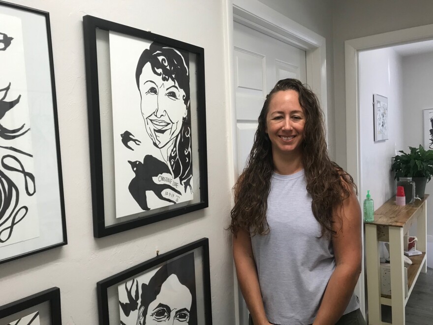 Springhill Therapeutic Massage owner Stacey Hyers poses next to a portrait of close friend and breast cancer survivor, Christine Bruton. (Molly Chepenik / WUFT)