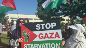 A group of people carry red, white, black and green flags and two people hold a sign saying “stop gaza starvation.”