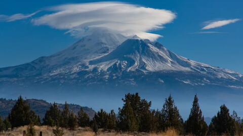 Lenticular clouds form layered, saucer-like shapes above snow-covered Mount Shasta.