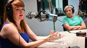Two women sit in a radio studio. The woman on the left is talking and gesturing with both hands.