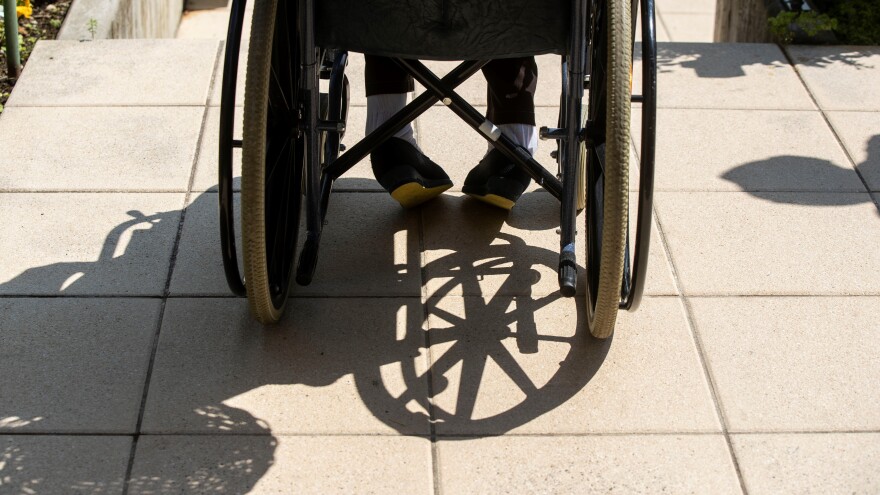 Wheelchair moving ahead of the picture, shadow being cast on the ground next to it.