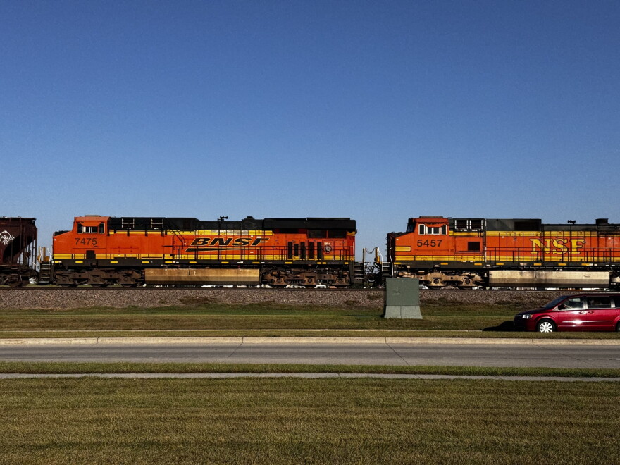 Two orange train cars with the BNSF and NSF logos ride along the train tracks on the side of a road.