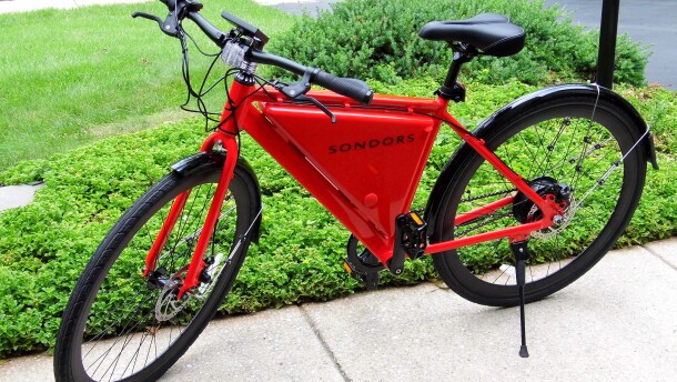 A red E bike parked on a sidewalk next to some green bushes.