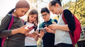Group of kids hang out in the street after school and using smart phones on a sunny day