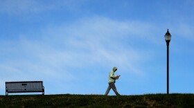 A lone man looks at his phone as he walks through a mostly empty park in Kansas City, Mo. Tuesday, April 14, 2020 as stay-at-home orders continue in much of the country in an effort to stem the spread of the new coronavirus. (AP Photo/Charlie Riedel)