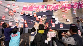 South Korean protesters attach stickers on a banner showing the Strait of Hormuz during a rally against the U.S. and Israel attacks on Iran near the presidential office in Seoul, South Korea, Saturday, March 28, 2026. The letters read "Refuse sending troops to Hormuz!" (AP Photo/Ahn Young-joon)
