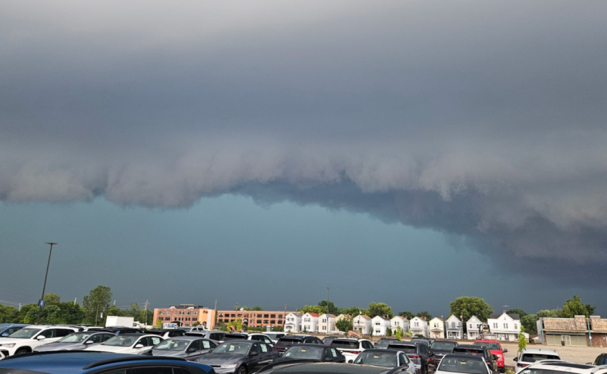 A line of dark storm clouds over a parking lot and several buildings