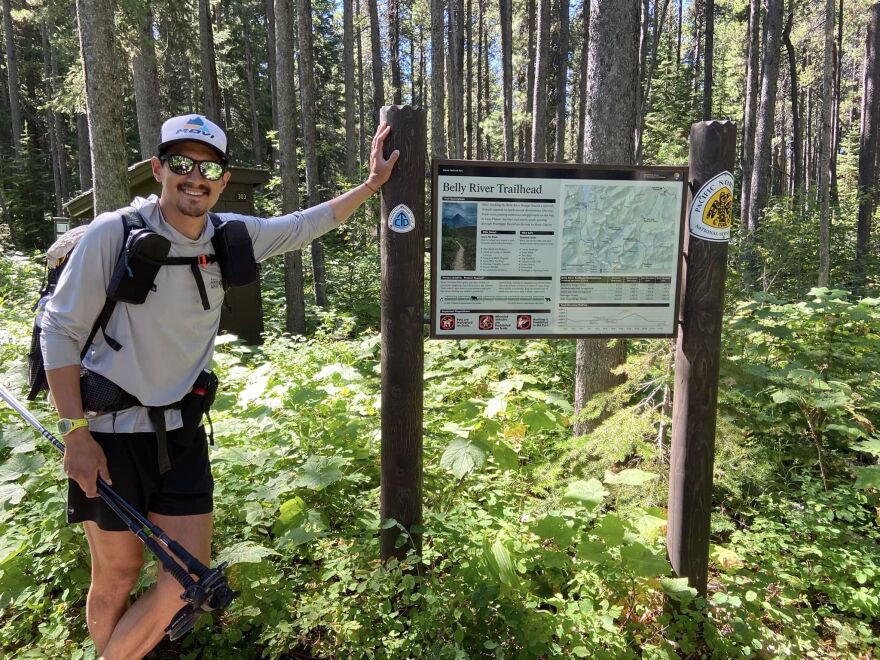 A man leans on a trailhead sign in a national forest.