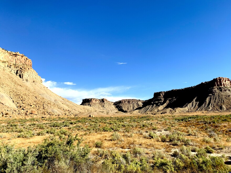 A lanscape view of tall plateaus against a blue sky. Green shrubs are on the ground.
